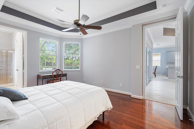 bedroom with ensuite bath, hardwood / wood-style flooring, baseboards, visible vents, and crown molding