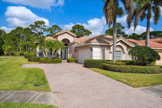 mediterranean / spanish-style house with stucco siding, decorative driveway, a tile roof, a front lawn, and an attached garage