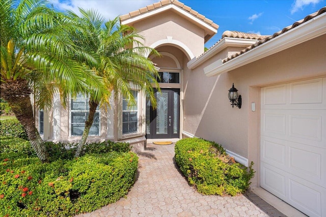 view of exterior entry featuring an attached garage, a tile roof, and stucco siding