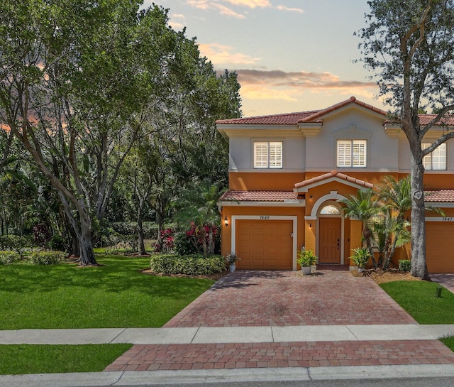 mediterranean / spanish home featuring a garage, decorative driveway, stucco siding, a tiled roof, and a lawn