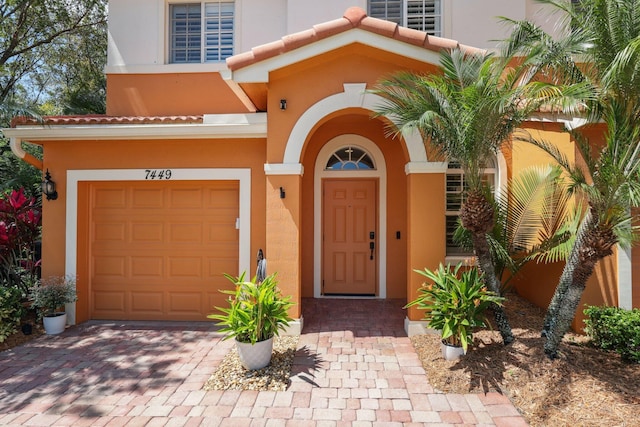 entrance to property featuring a garage, stucco siding, and decorative driveway