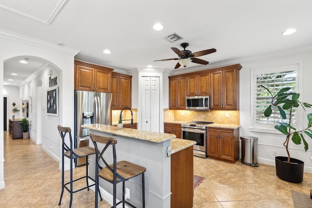 kitchen featuring visible vents, a breakfast bar, brown cabinets, tasteful backsplash, and appliances with stainless steel finishes