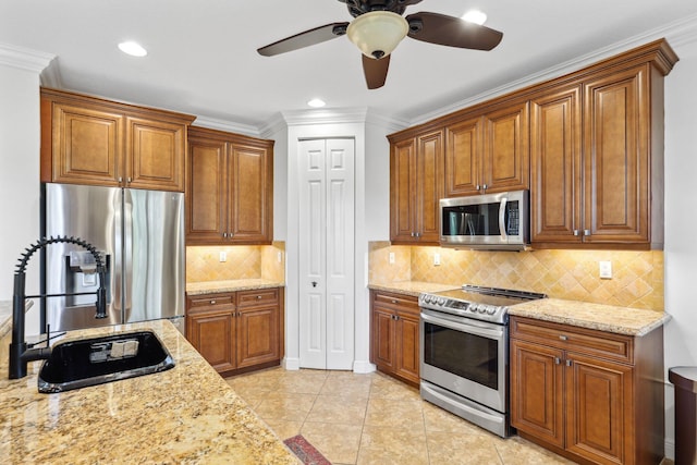kitchen featuring brown cabinets, light stone countertops, stainless steel appliances, a ceiling fan, and tasteful backsplash