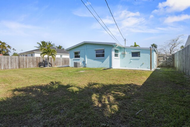 rear view of house with stucco siding, a yard, a fenced backyard, and central AC