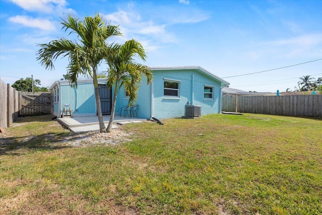rear view of property with a fenced backyard, a yard, central AC, and stucco siding