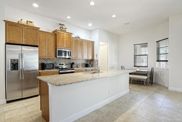 kitchen featuring baseboards, a sink, decorative backsplash, a center island with sink, and stainless steel appliances
