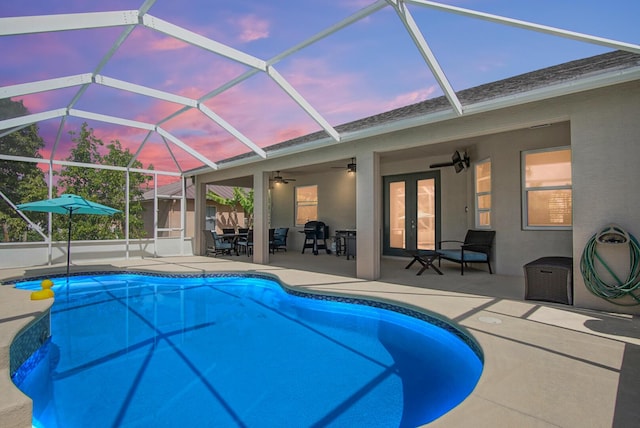 pool at dusk with a patio, french doors, a ceiling fan, an outdoor pool, and glass enclosure