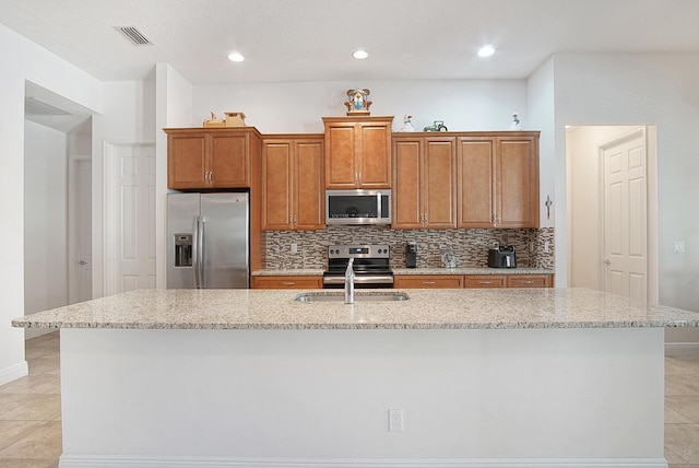 kitchen with a sink, stainless steel appliances, a kitchen island with sink, visible vents, and backsplash
