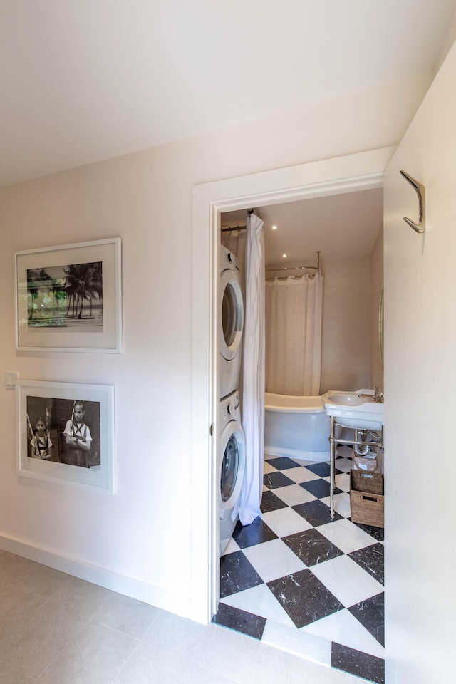 washroom with stacked washer / drying machine, a sink, tile patterned floors, laundry area, and baseboards