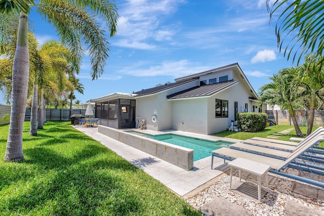 back of property featuring a lawn, a standing seam roof, stucco siding, a sunroom, and a fenced backyard