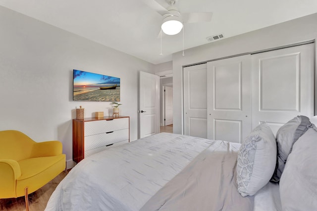 bedroom with a closet, wood finished floors, visible vents, a ceiling fan, and baseboards