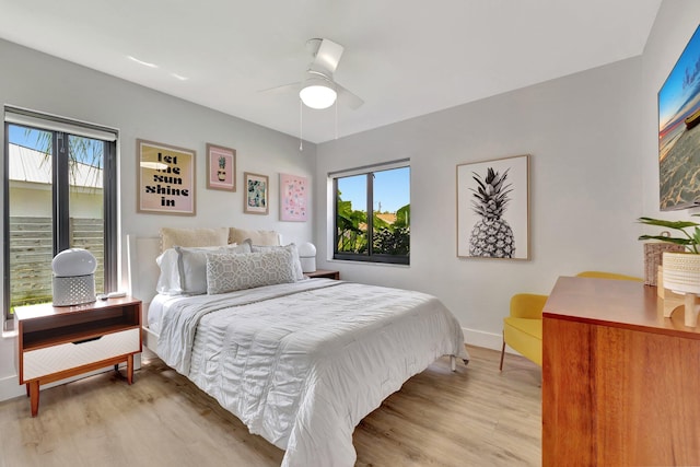 bedroom featuring ceiling fan, baseboards, multiple windows, and light wood-style floors