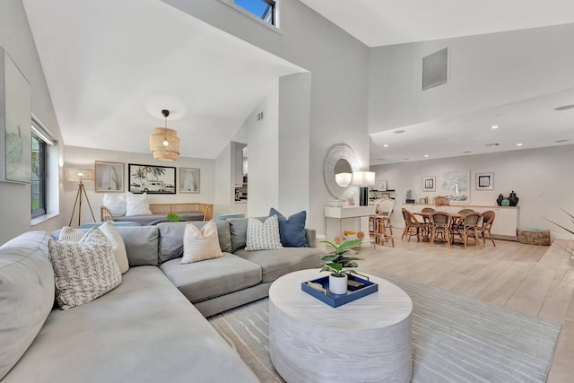 living area with recessed lighting, light wood-style floors, visible vents, and a high ceiling