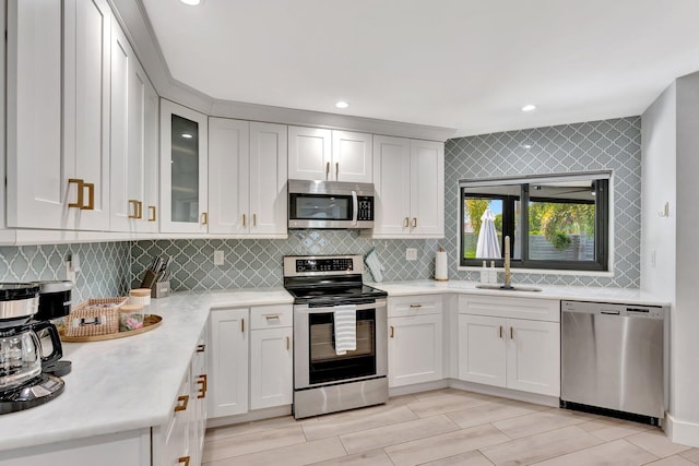 kitchen with glass insert cabinets, a sink, light countertops, tasteful backsplash, and appliances with stainless steel finishes