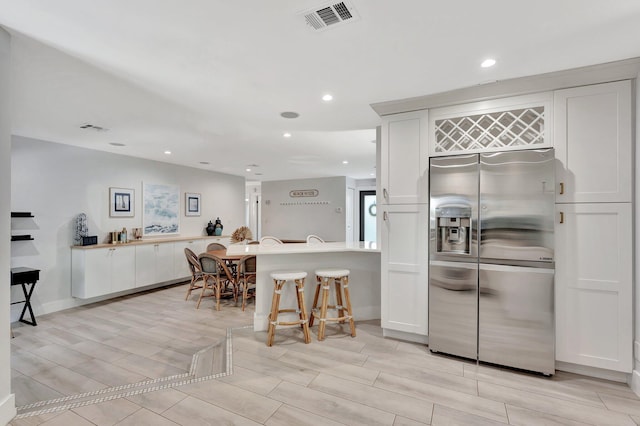 kitchen featuring stainless steel fridge with ice dispenser, a kitchen bar, visible vents, and wood tiled floor
