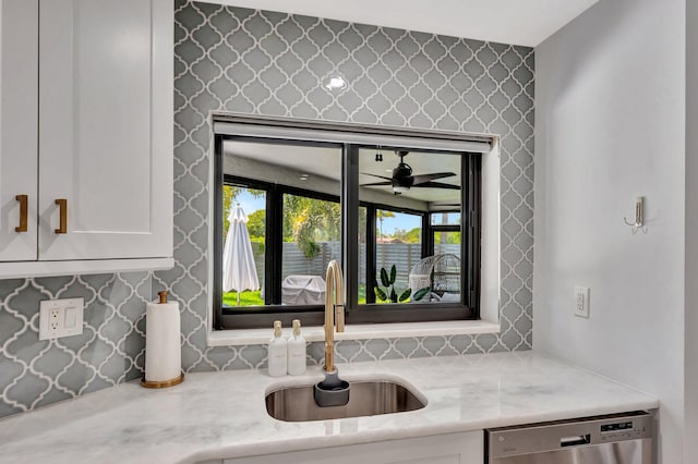 interior space featuring white cabinetry, stainless steel dishwasher, light stone countertops, and a sink