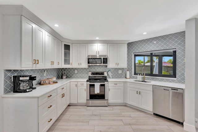 kitchen with a sink, stainless steel appliances, white cabinets, light countertops, and decorative backsplash