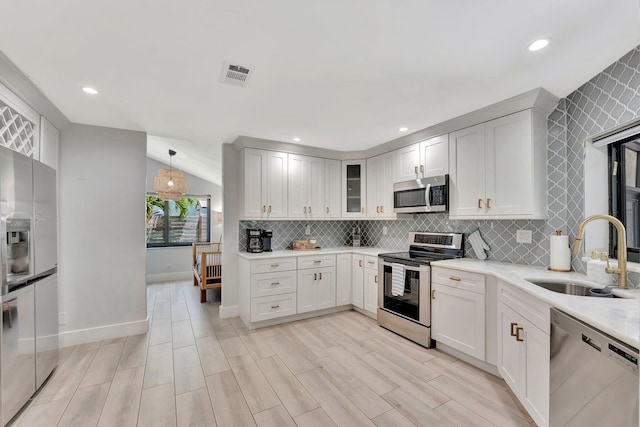kitchen featuring stainless steel appliances, baseboards, a sink, decorative backsplash, and light countertops