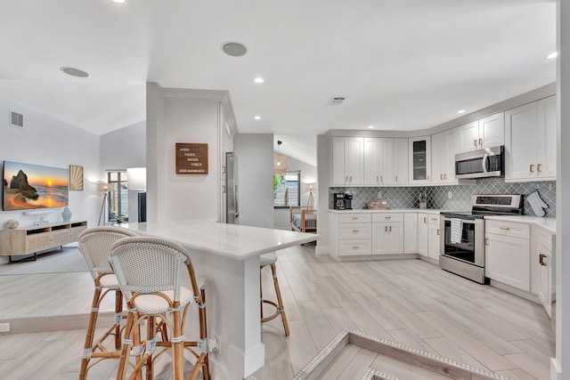 kitchen with a peninsula, a breakfast bar, stainless steel appliances, visible vents, and tasteful backsplash