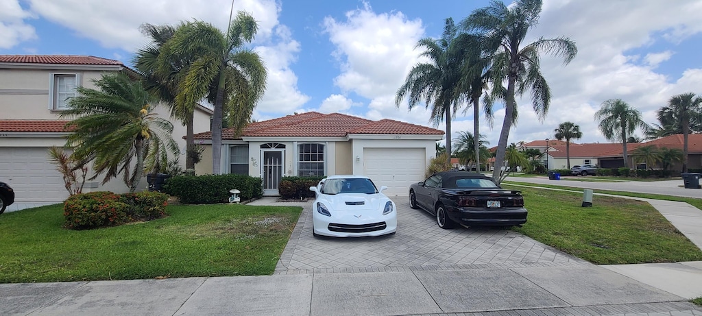 mediterranean / spanish-style home with decorative driveway, a front lawn, a tiled roof, a garage, and stucco siding