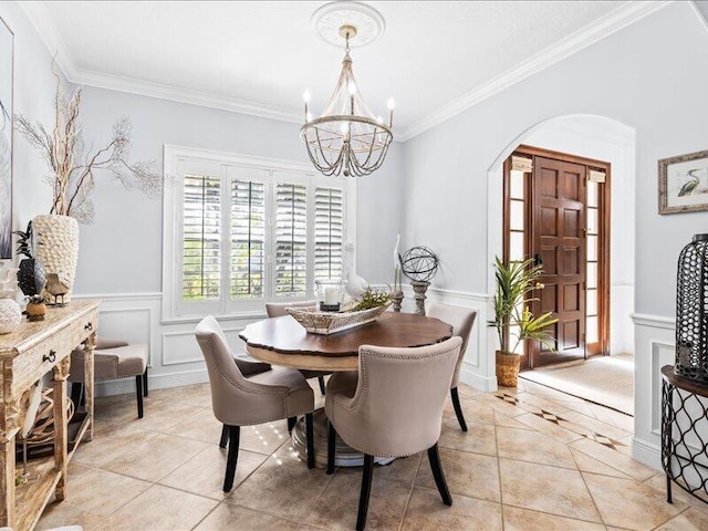 dining space with an inviting chandelier, crown molding, a wainscoted wall, arched walkways, and light tile patterned floors
