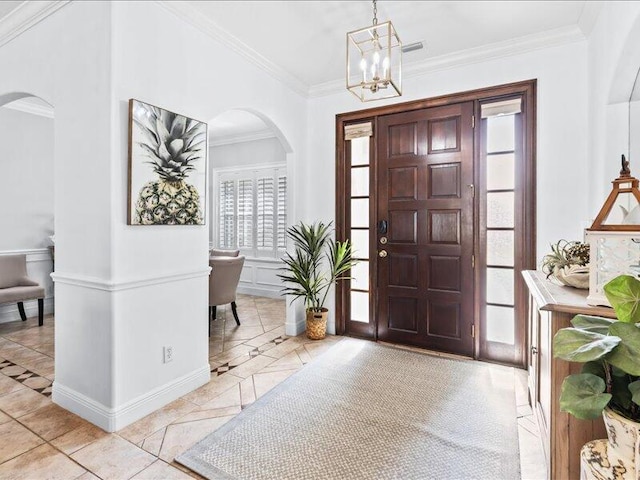 foyer entrance with crown molding, arched walkways, baseboards, and a chandelier
