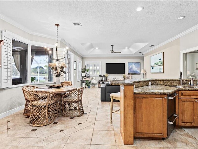 kitchen with brown cabinetry, crown molding, visible vents, dark stone counters, and a sink