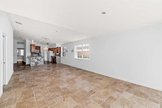 unfurnished living room featuring baseboards, visible vents, and stone finish floor