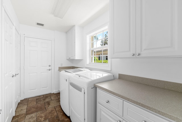 laundry area with visible vents, cabinet space, washing machine and dryer, and stone tile flooring