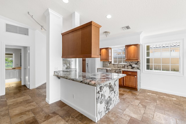 kitchen with baseboards, brown cabinetry, stone tile flooring, and visible vents