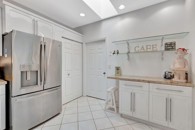 kitchen with white cabinets, a skylight, light tile patterned flooring, and stainless steel fridge with ice dispenser