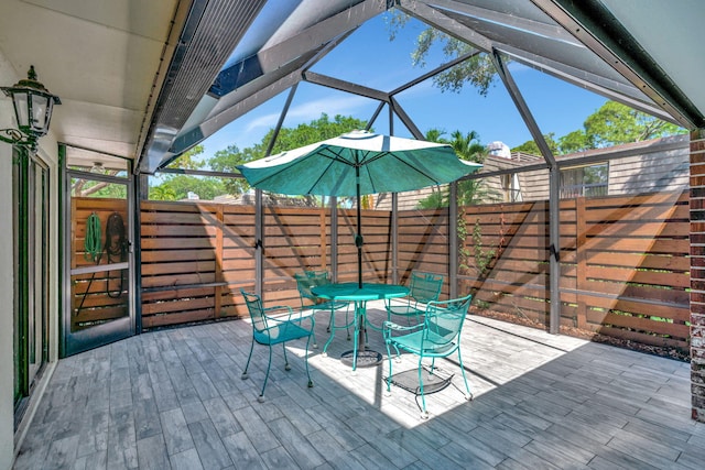 view of patio / terrace featuring glass enclosure, fence, a wooden deck, and outdoor dining space