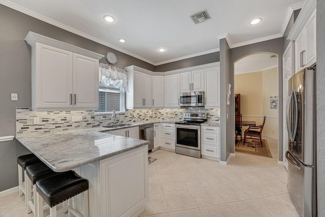 kitchen featuring visible vents, a sink, arched walkways, a peninsula, and appliances with stainless steel finishes