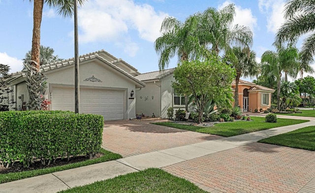 view of front facade featuring decorative driveway, a front lawn, a tiled roof, a garage, and stucco siding
