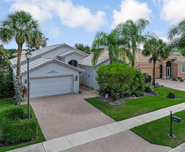 view of front of home with a tiled roof, stucco siding, decorative driveway, a front yard, and a garage