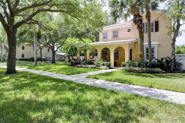 mediterranean / spanish house with a tiled roof, a front yard, and stucco siding