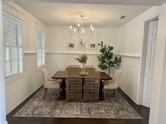 dining space with wood finished floors, visible vents, a textured ceiling, and a notable chandelier