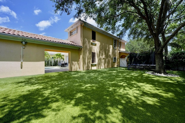 back of house featuring a lawn, a tile roof, a trampoline, and stucco siding