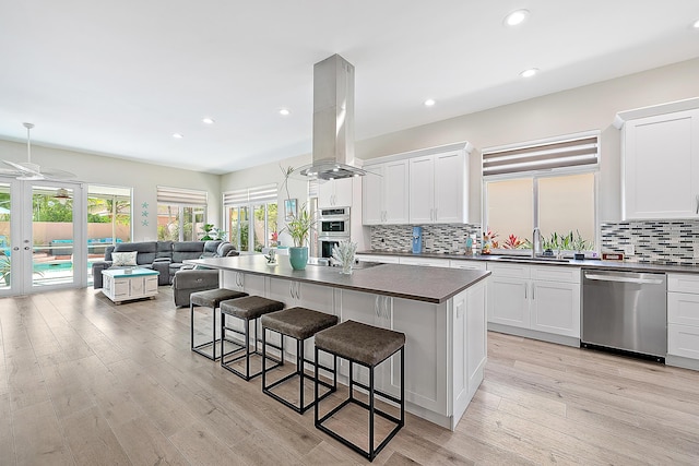 kitchen with dark countertops, a kitchen breakfast bar, stainless steel appliances, open floor plan, and island range hood