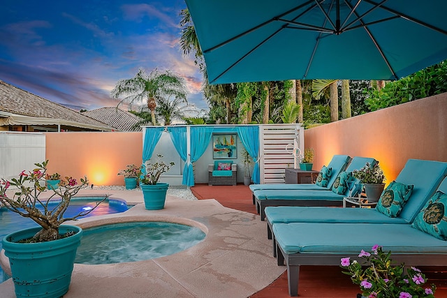 pool at dusk featuring a deck, fence, and a jacuzzi