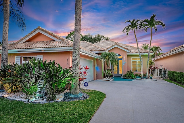 mediterranean / spanish house featuring an attached garage, fence, stucco siding, and a tile roof
