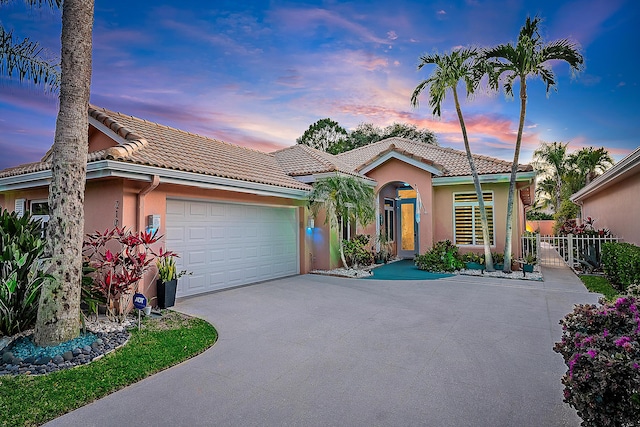 view of front of house with driveway, a tile roof, a garage, fence, and stucco siding