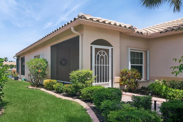 view of exterior entry with stucco siding, a lawn, and a tile roof