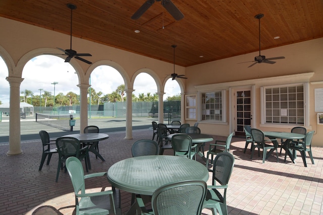 view of patio / terrace featuring a tennis court, a ceiling fan, outdoor dining space, and fence
