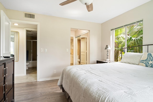 bedroom with visible vents, wood finished floors, baseboards, ceiling fan, and ensuite bath