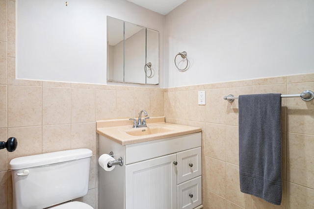 bathroom with toilet, tile walls, wainscoting, and vanity