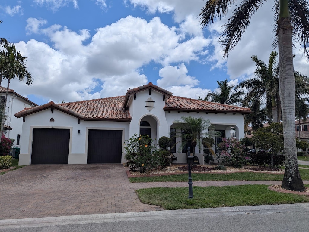mediterranean / spanish-style home featuring a garage, stucco siding, decorative driveway, and a tiled roof