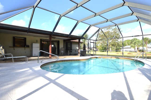outdoor pool with ceiling fan, glass enclosure, and a patio