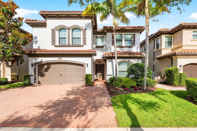 mediterranean / spanish house featuring a garage, a front yard, decorative driveway, stucco siding, and a tile roof