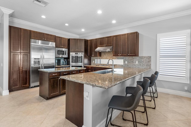 kitchen featuring visible vents, a center island, built in appliances, under cabinet range hood, and light tile patterned flooring